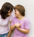 Junge Frau und Mädchen mit Down-Syndrom stehen neben einander und lächeln sich an